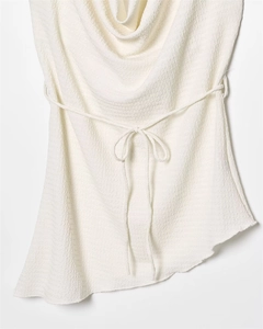 Detail of white cowl neck top with unique pleated texture and irregular asymmetric hemline