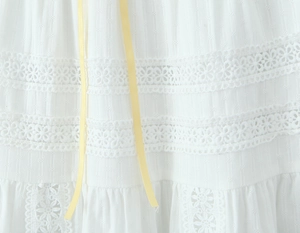 Detail of white jacquard fabric with delicate lace flowers and a yellow satin ribbon