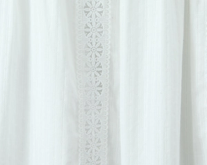 Detailed close-up of white fabric with vertical lace embroidery and floral cut-outs