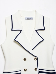 Detail of white sleeveless knit vest with navy trim and decorative gold buttons