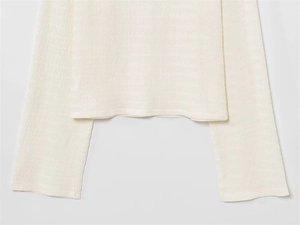 Vue détaillée de la texture ondulée fine et des poignets évasés sur un haut blanc cassé