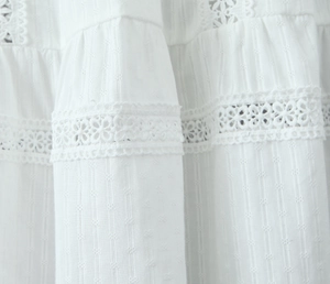 Close-up of white cotton fabric featuring delicate floral lace inserts and textured stripes