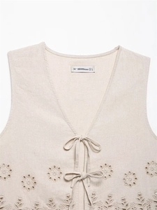Detailed view of beige linen vest featuring V-neck ties and floral cutout embroidery