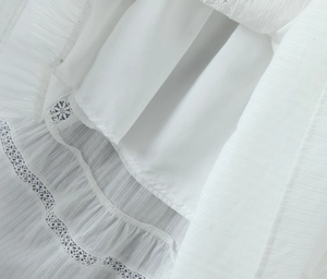 Detail of white sleeveless top with floral lace patchwork and pleated texture fabric