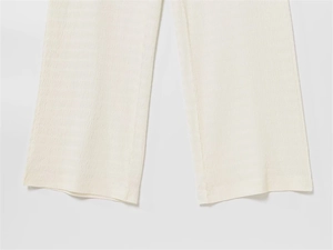Vue détaillée de la texture du tissu plissé beige et de la couture de ce pantalon