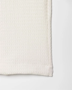 Close-up of white seersucker fabric texture and fine stitching on irregular tie-up top