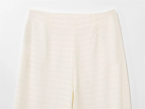 Détail du pantalon plissé blanc crème avec taille minimaliste et textures ondulées