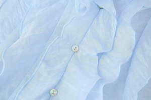 Detail of light blue chiffon top featuring layered ruffles and pearlescent white buttons