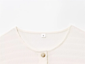Détail du col en tissu texturé avec bouton marbré et étiquette de taille S blanc