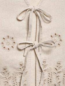 Detail of beige linen vest featuring intricate eyelet embroidery and tie-front bows