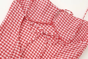 Detail of red gingham dress showing delicate straps and pleated fabric texture