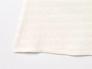 Vue détaillée de la texture du tissu plissé blanc avec motif ondulé vertical sur le vêtement