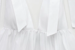 Detailed close-up of white poplin top featuring deep V-neck and fine pleated bust line