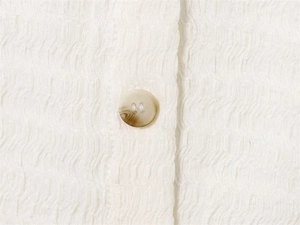 Détail du tissu seersucker texturé et d'un bouton marbré sur une chemise blanche