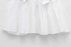 Close-up of white poplin fabric showing tiered ruffle hem and delicate bow decoration