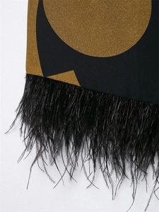 Macro detail of geometric print fabric with black feather fringe and gold-brown tones