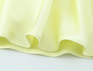 Close-up of light yellow satin dress showing smooth fabric texture and neat hemline stitching
