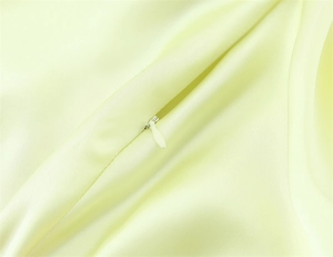 Detailed view of concealed zipper on light yellow satin dress with smooth fabric texture