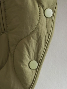 Close-up of olive green quilted vest showing matte buttons and side slit stitching