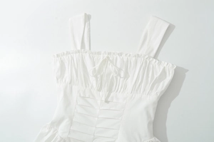 Détail de robe blanche avec encolure à volants, nœud à cordon et texture en tissu plissé