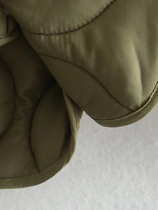 Detail of olive green quilted fabric with fine stitching and side slit on women's cotton jacket