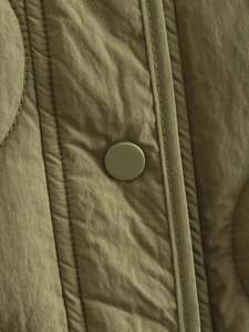 Close-up of olive green quilted jacket featuring side slit and matching resin snap button