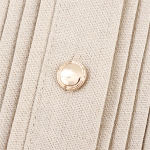 Gros plan d'un bouton métallique doré sur le tissu en lin plissé beige de la robe