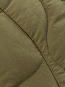Detailed view of olive green quilted fabric with fine twill texture and neat stitching