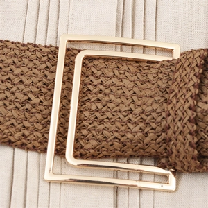 Gros plan sur une ceinture tressée marron avec boucle en métal doré sur robe plissée