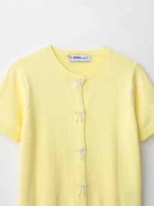 Detail of yellow knit cardigan with faux pearl bows and ribbed round neckline