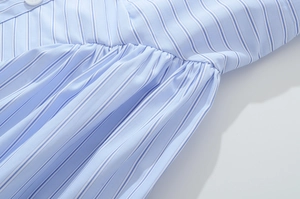 Detail of light blue striped fabric featuring ruffled pleats and a white round button