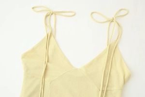 Detail of light yellow V-neck dress featuring adjustable bow tie straps and textured fabric