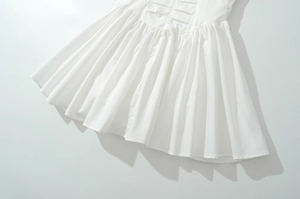 Vue détaillée de l'ourlet plissé de la robe blanche avec coutures fines et coton