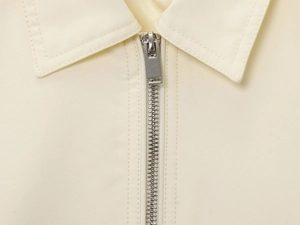 Detail shot of a minimalist cream bomber jacket featuring a silver metal zipper and collar