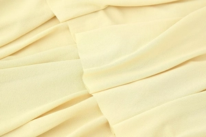 Macro detail of lightweight pale yellow chiffon fabric with fine textured fringe and pleats