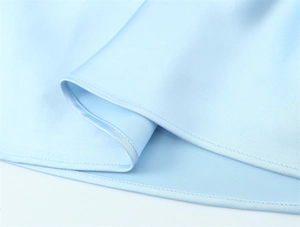 Detailed close-up of smooth light blue satin fabric with precise stitching on the hem
