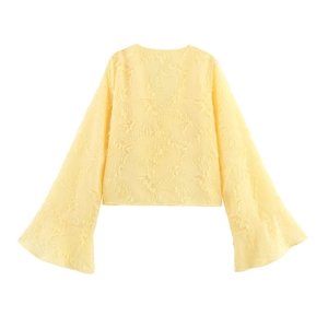 Détail d'un chemisier jaune clair à manches longues avec texture à franges et manches cloche