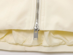 Detailed close-up of the silver metal zipper and woven fabric on the cream bomber jacket