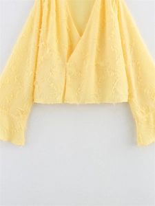 Détail du haut court jaune à manches longues avec un tissu texturé unique effet plumes