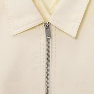 Close-up of minimalist cream bomber jacket featuring silver metal zipper and sharp collar