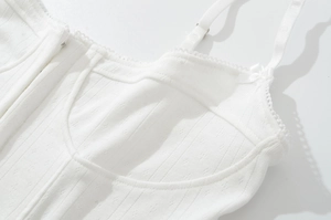 Détail d'un caraco blanc montrant le tissu pointelle, la dentelle et le nœud sur bretelle