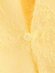 Détail du tissu jacquard jaune clair avec texture à franges et un bouton rond assorti
