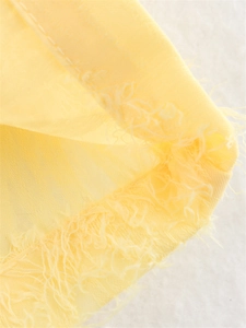 Détail macro du tissu jaune clair transparent avec bords effilochés et coutures précises