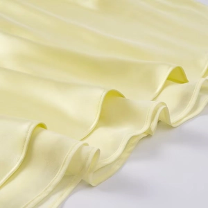 Macro detail of soft cream yellow satin fabric featuring ruffled hem and fine stitching