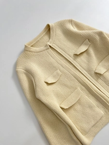 Dettaglio del cardigan in maglia crema con tessuto strutturato e quattro tasche decorative