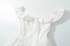 Détail de l'encolure à volants avec nœud et dentelle sur une robe blanche d'été