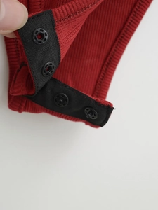 Détail du body en tissu côtelé rouge avec quatre boutons-pression en métal noir