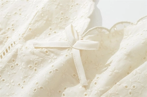 Détail de l'encolure festonnée avec broderie florale et nœud en satin sur robe crème