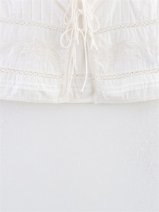 Close-up of white bohemian camisole with floral embroidery and lace-up details