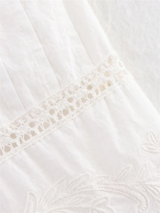 Detail of white cotton camisole featuring delicate lace inserts and floral embroidery